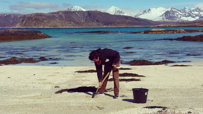 researcher digging for worms in on beach sand, sea and mountains in background