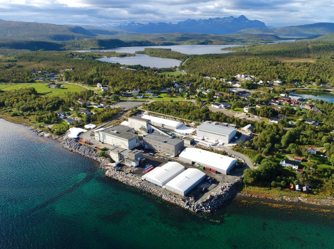 picture of the processing plant in Tysfjord, with a gren landscape and mountains in the background