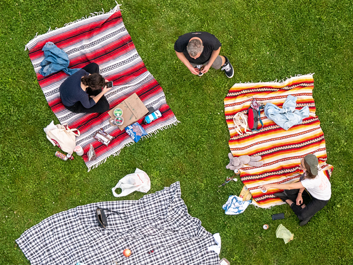 Personer nyter piknik på pledd på gresset sett ovenfra. 