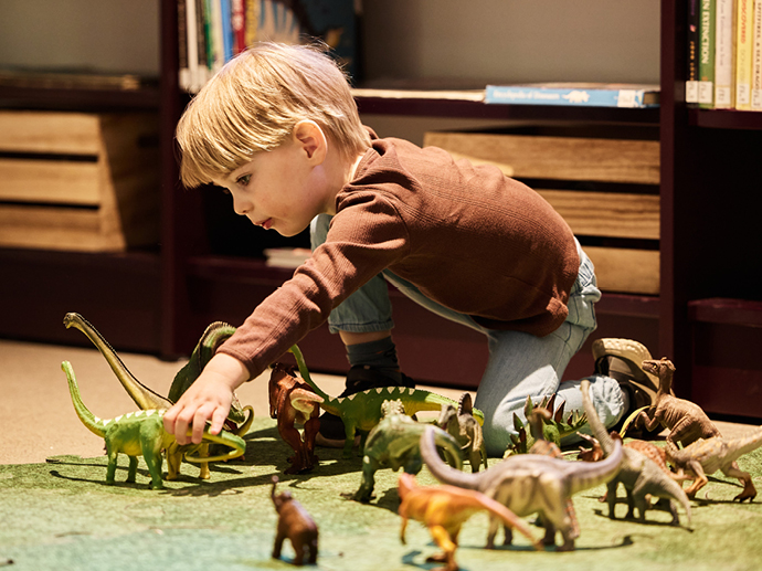 Liten gutt leker med små figurer av dinosaurer.